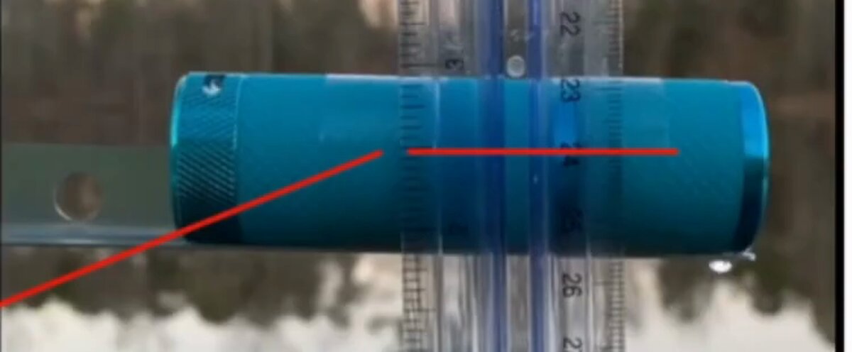 Close view of the target: a small blue anodised flashlight or torch resting on a metal bracket at the pond's edge.