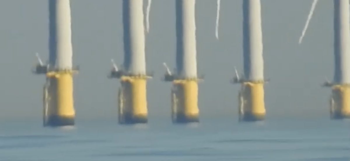 Five turbine bases in a row, each vertically smeared and stretched near the yellow transition piece, with dark compressed bands beneath and a bright hazy strip at the waterline.