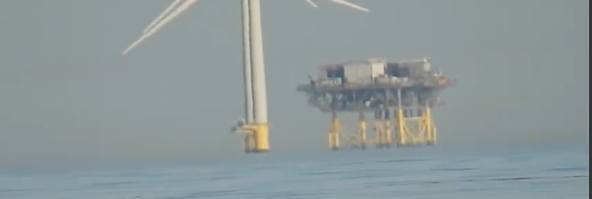 A turbine and the offshore substation platform on jacket legs, both appearing lofted above a gap of haze over the sea — a looming effect.